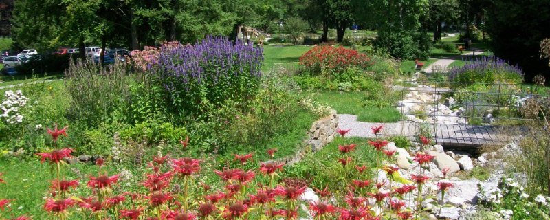 Üppige Blütenpracht und alter Baumbestand im Parkgelände, den ein kleiner Bachlauf mit kleinen Brücken durchzieht., © Gästeinformation Bad Heilbrunn