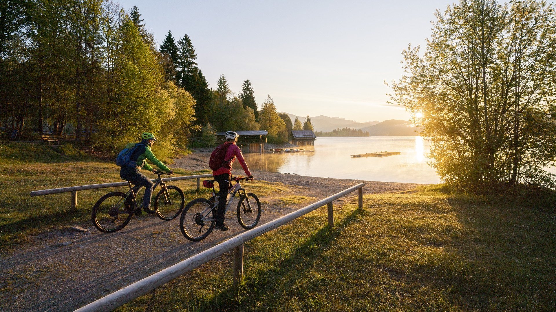 Welch Ausblick auf den Walchensee! Zwei Fahrradfahrer fahren auf den in morgendlichen Sonnenlicht getauchten Walchensee zu., © Archiv Tölzer Land Tourismus| Foto: Bernd Ritschel